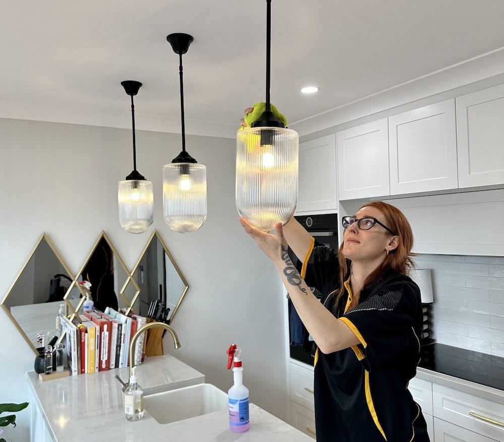 Maria dusting lights in kitchen with yellow microfibre cloth