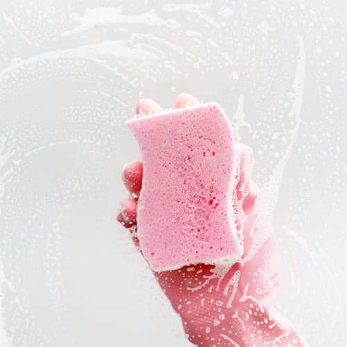 clear glass in soapy foam, a hand in a pink glove and a sponge washes the glass
