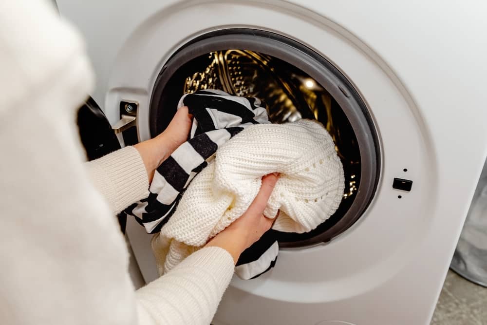 Woman putting white clothes into the drum of a washing machine