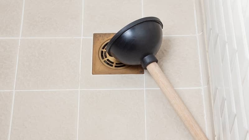 Rubber plunger with wooden handle on the shower floor.