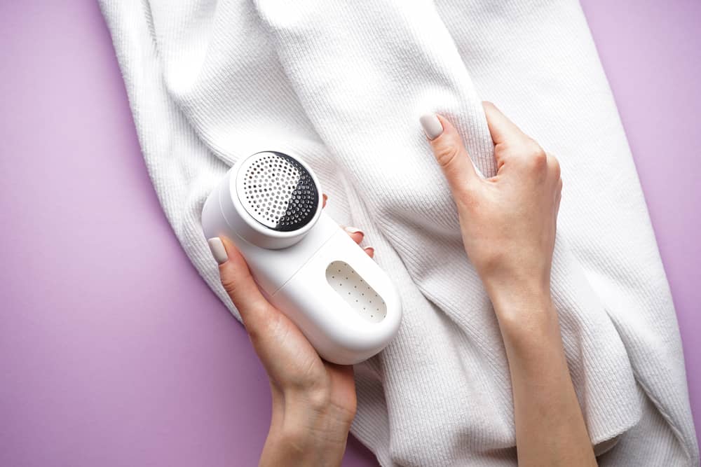 Female hand with modern fabric shaver and clothes and wool sweater.