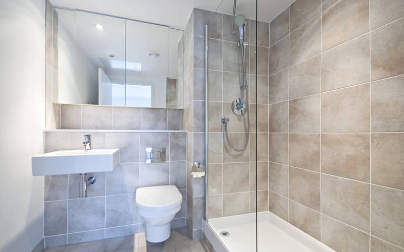 Modern en suite bathroom with large shower, toilet and wash basin in beige natural with natural stone tiled walls.