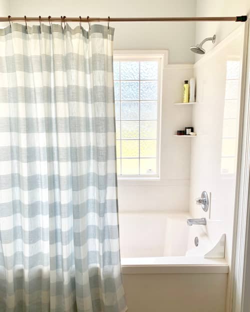 Light blue gingham pattern shower curtain, white marble shower and a large window for natural light.