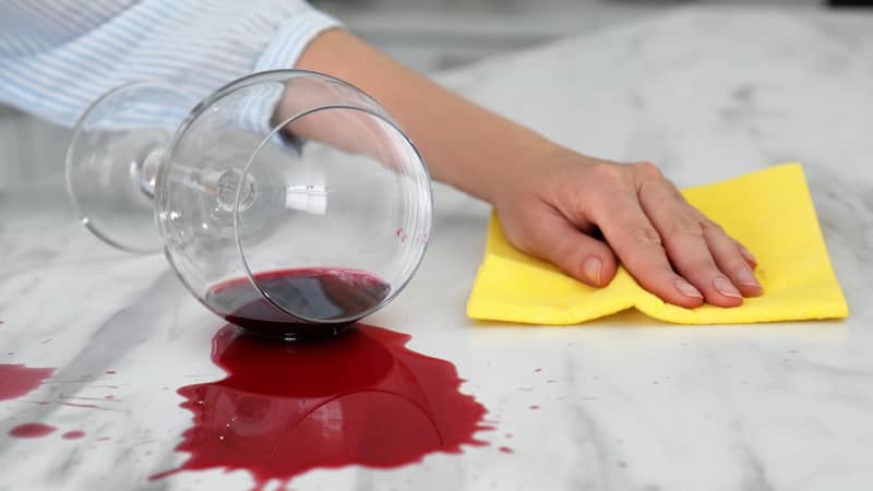 Woman cleaning spilled wine on white marble table indoors, closeup