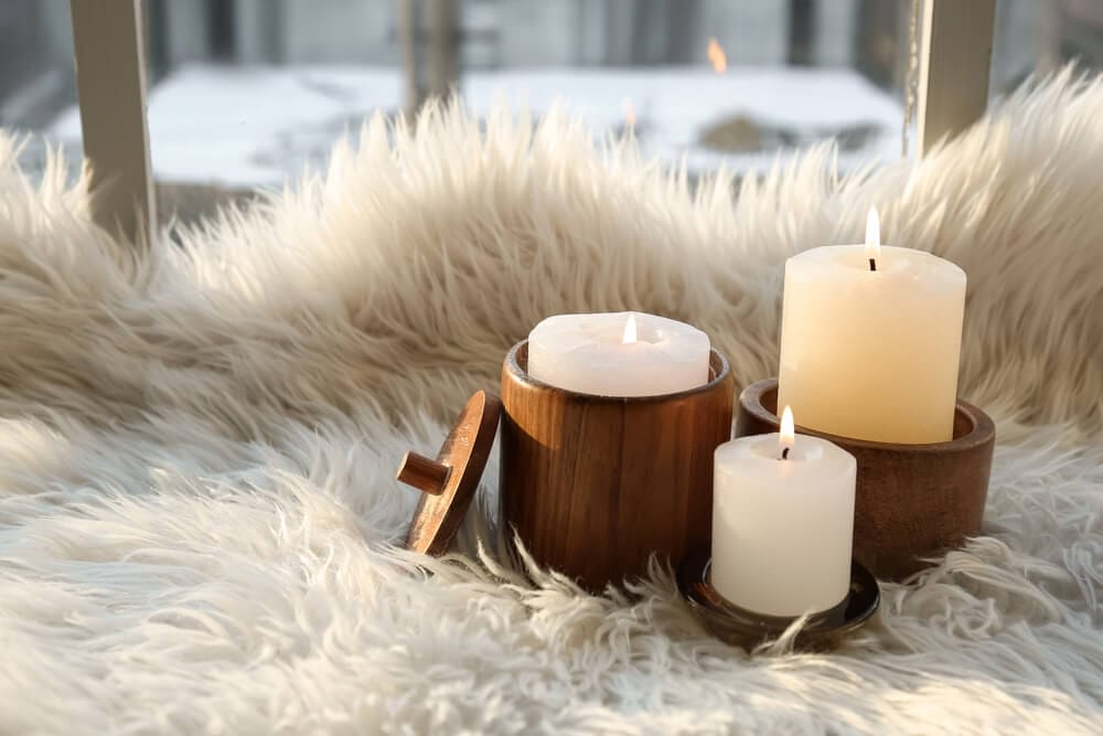 Holders with burning candles on fur carpet near window.