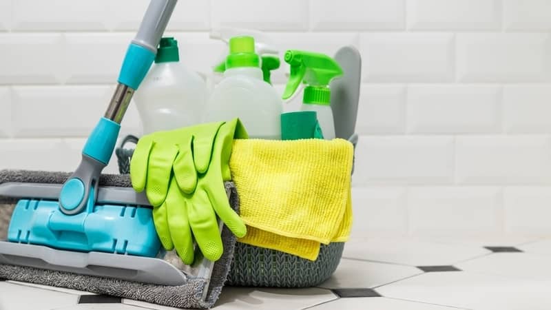 Basket with cleaning products on white ceramic tile floor in bathroom.