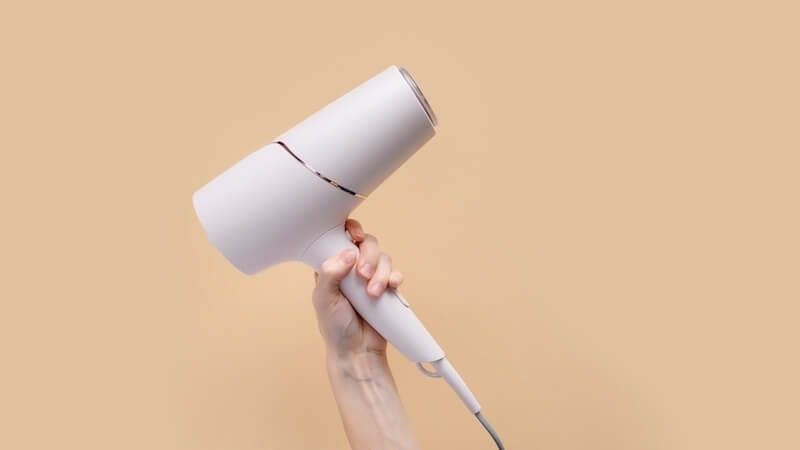 White plastic hair dryer in hand on a beige background.