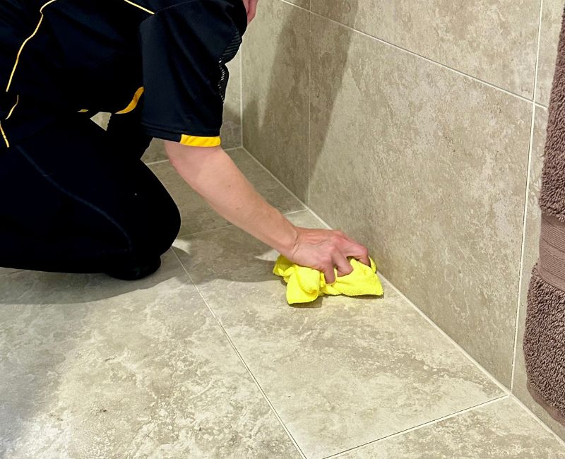 house-cleaner-cleaning-natural-stone-shower-floor Professional cleaner using cloth to clean natural stone shower floor