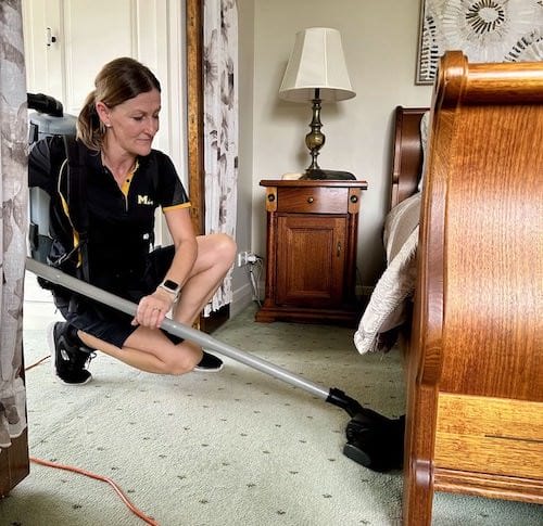 Maid2Match professional cleaner Lia vacuums under a customer's bed