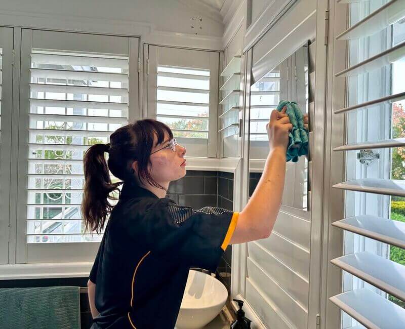 House cleaner Tullie wiping bathroom mirror with microfibre cloth