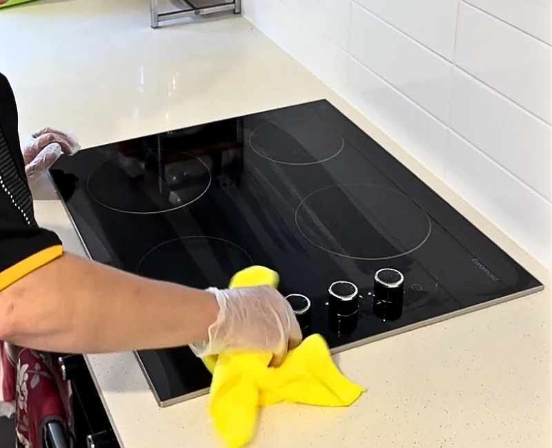 professional cleaner wiping electric stove knobs with yellow microfibre cloth