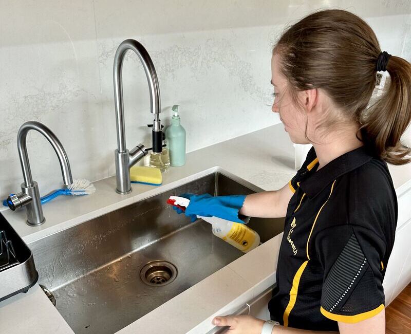 Maid2Match cleaner Jade spraying the stainless steel in the kitchen sink