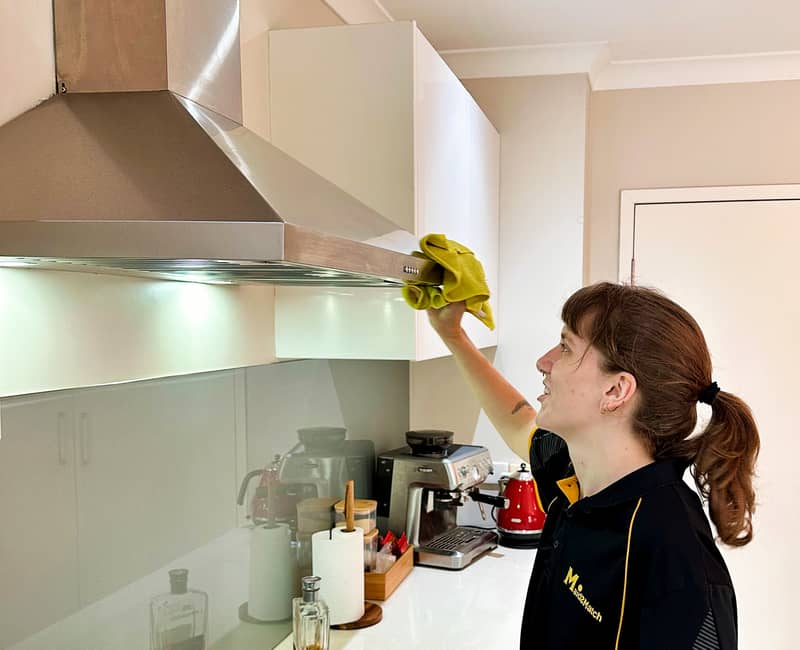 Maid2Match expert cleaner Kayleigh wiping the surface of a stainless steel rangehood in the kitchen