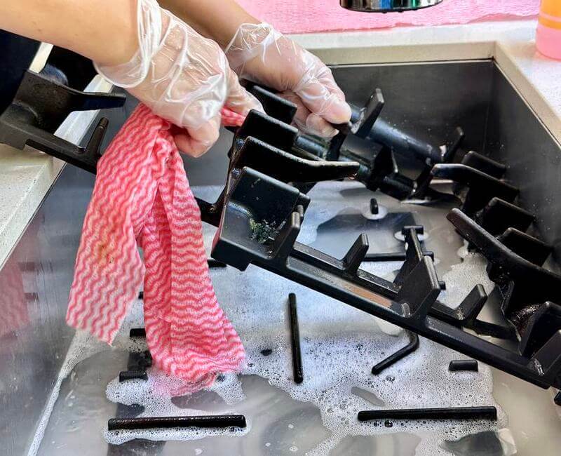 Hand of a professional cleaner wearing protective rubber gloves cleaning stovetop grates