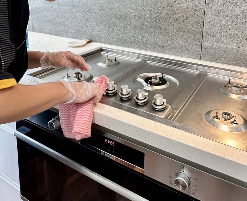 Expert house cleaner wiping the knobs of a stove top