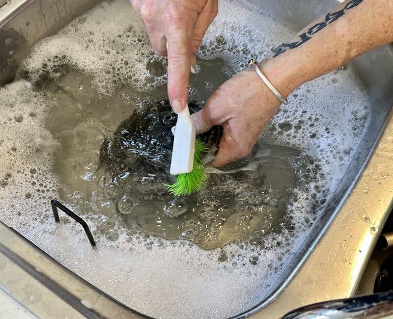 Maid2Match expert cleaner scrubbing the burner cap of a stainless steel cooktop with a brush