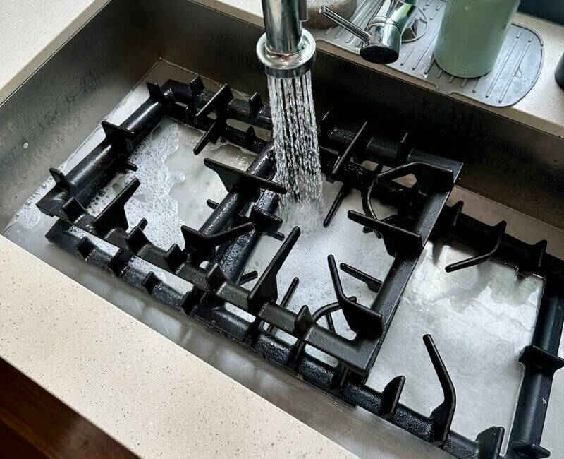 Stovetop grates placed on the sink with soap and running water for cleaning