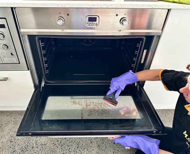 Maid2Match expert house cleaner using cooktop scraper to clean oven glass