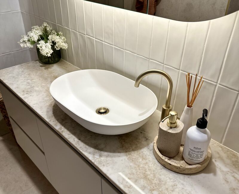 Clean bathroom sink on top of a marble benchtop inside a bathroom with cream-colored tiles
