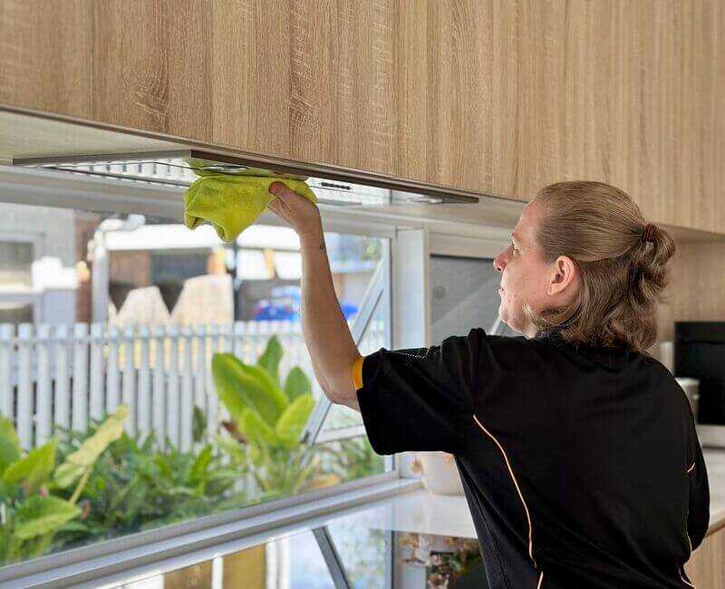 House cleaner cleaning rangehood surface with microfibre cloth