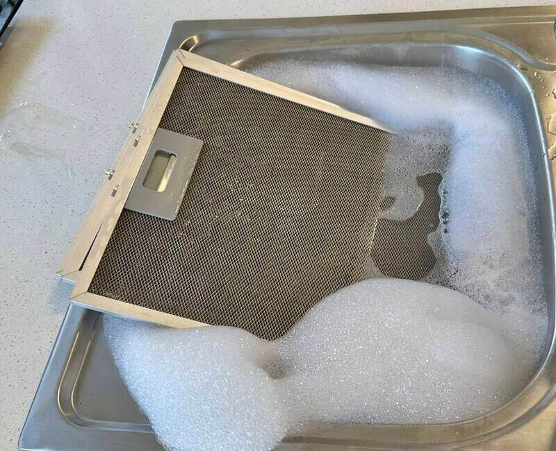 rangehood filter submerged in soapy water in the kitchen sink