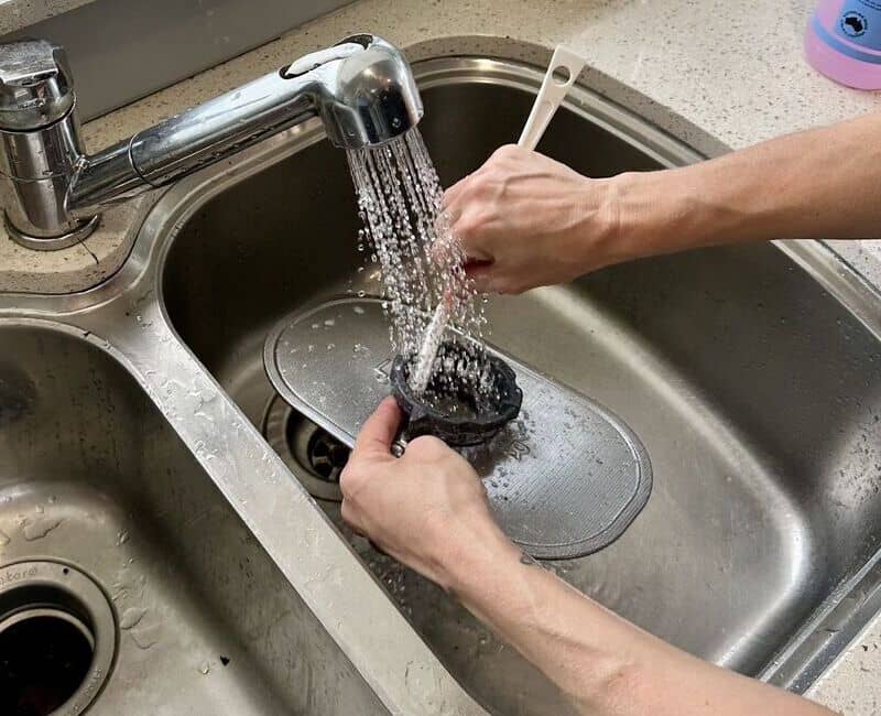 cleaning dishwasher filter using a soft brush under a running water in the sink