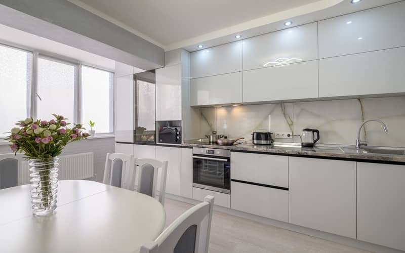 Interior of white modern kitchen with dining table and laminated cabinets