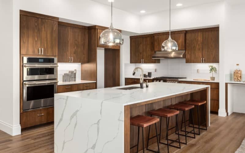 Luxury kitchen with quartz waterfall island, hardwood floors, dark wood cabinets, and stainless steel appliances