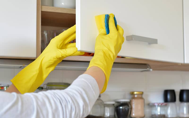 woman in yellow gloves cleaning the door in kitchen cabinet