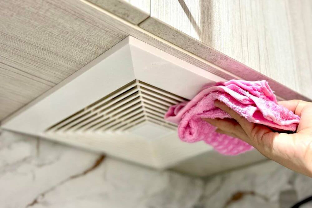 close up of hand wiping kitchen exhaust fan with pink microfibre cloth