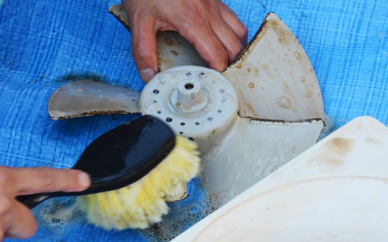 close up of hands using a brush to scrub greasy kitchen exhaust fan