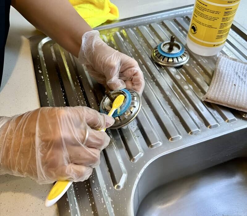 Maid2Match expert house cleaner scrubbing the strainer of kitchen sink with a toothbrush