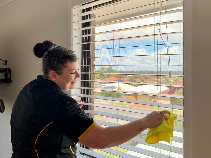 Maid2Match professional cleaner holding a yellow cloth and wiping the Venetian blinds