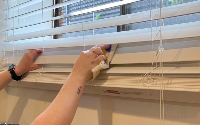 professional cleaner's hand holding white cloth wiping the Venetian blinds