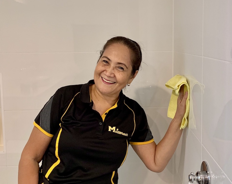 a Maid2Match professional cleaner smiling while cleaning the shower