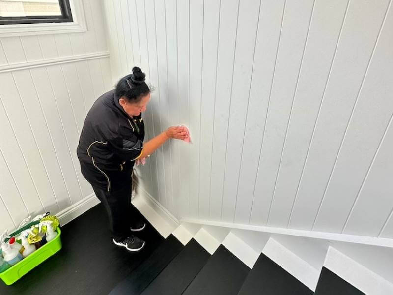 House cleaner Janet wipes white wooden walls with microfibre cloth