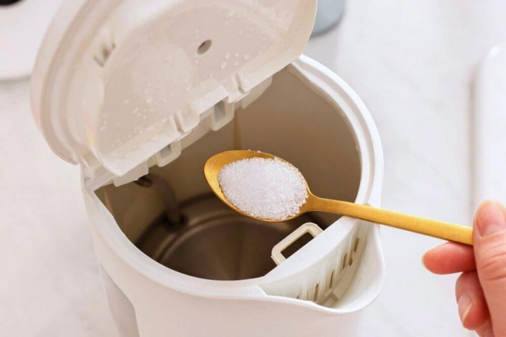 Spoonful of citric acid about to be poured in a kettle for cleaning