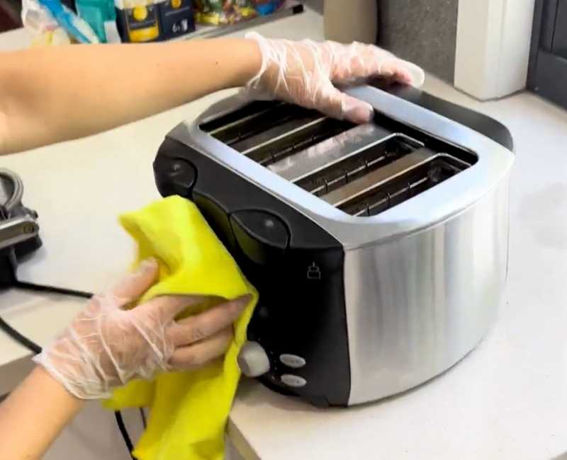 Professional cleaner with gloved hands cleans a toaster with a yellow microfibre cloth