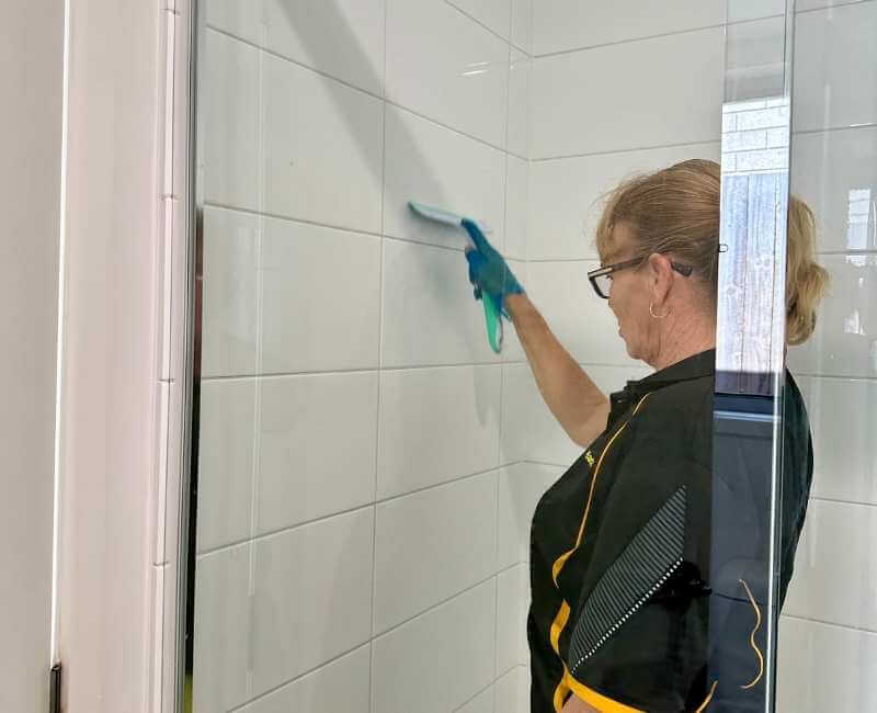 Maid2Match Brisbane Professional Cleaner, Elizabeth using squeegee to clean shower walls