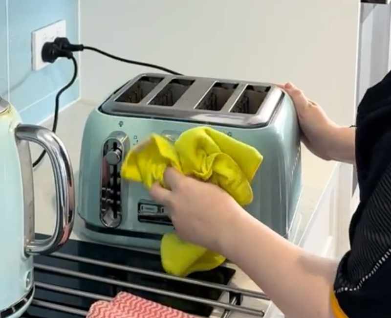Professional cleaner uses a yellow microfibre cloth to clean the outside surface of a toaster
