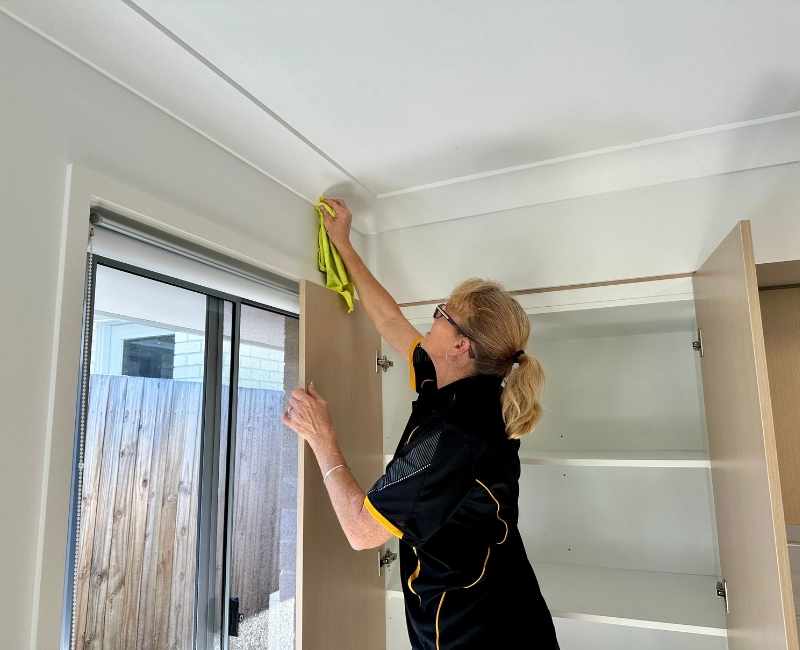 Maid2Match professional house cleaner and bond cleaner Elizabeth cleans a wall spot above the window near the ceiling