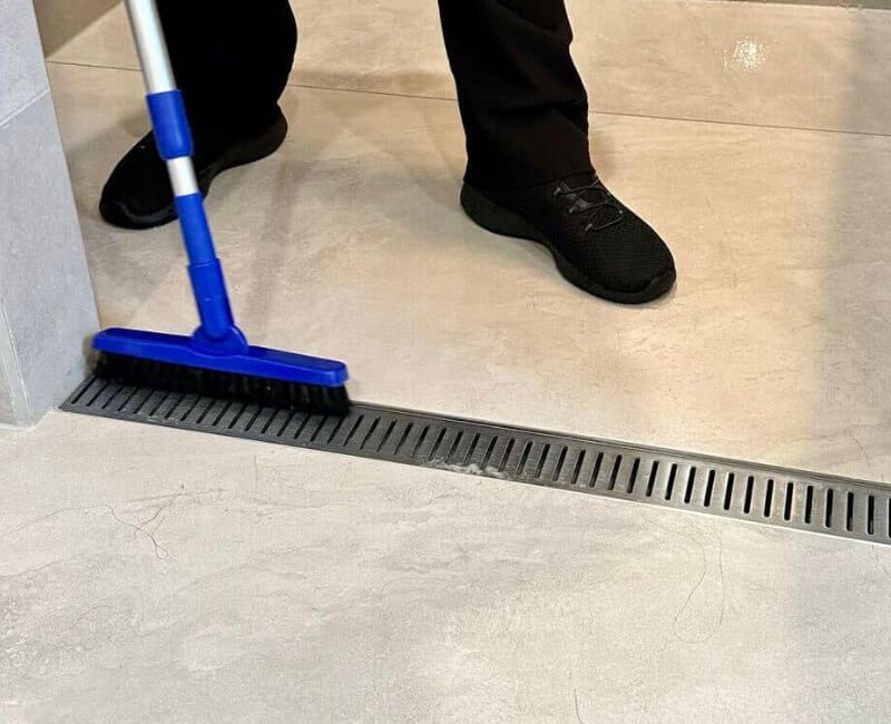 linear shower drain being cleaned with brush