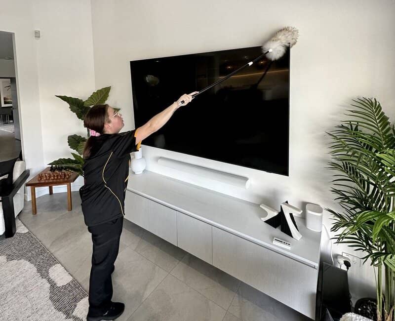 Kirsten cleaning television screen with a feather duster