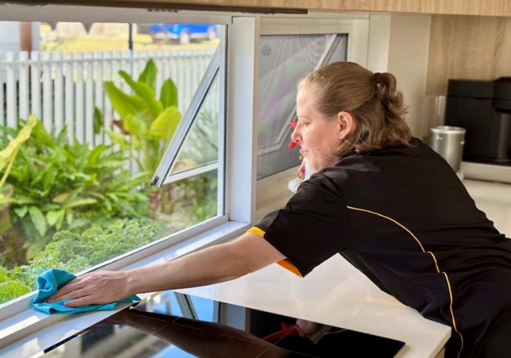 NDIS-professional-cleaner-Nicole-cleaning-window-interior Maid2Match professional cleaner, Nicole cleaning window interior near the kitchen stovetop