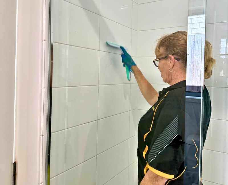 Maid2Match professional house cleaner Elizabeth uses squeegee to clean shower tiles
