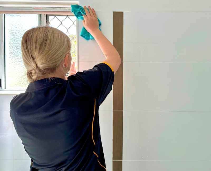 Maid2Match Brisbane house cleaner Casey cleans shower tiles in a bathroom with open window