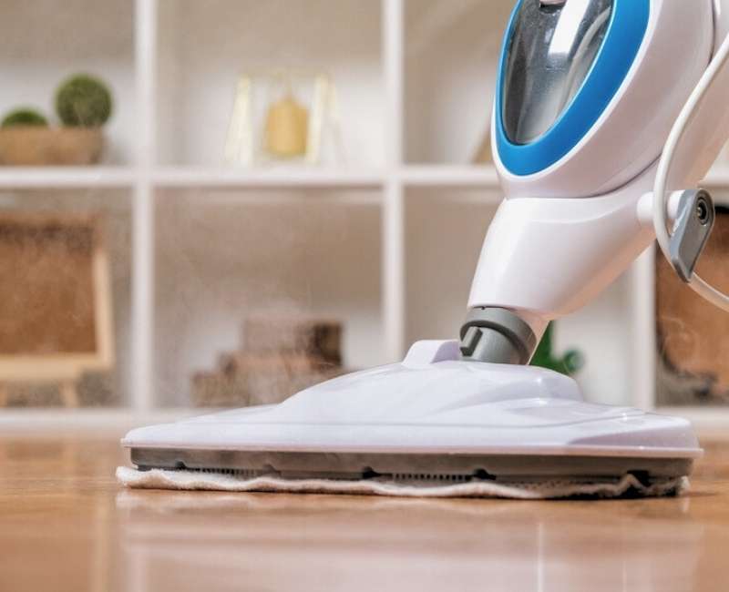 Cleaning with steam mop on wooden floor in the living room
