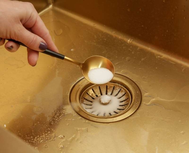 Pouring a spoon of baking soda on a kitchen sink drain to remove odours