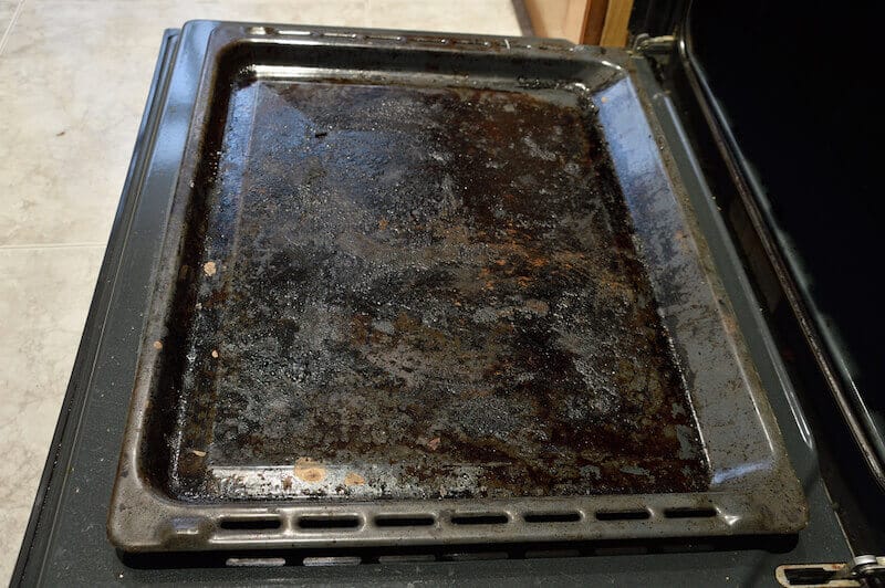Dirty oven tray with burnt food, oils, and discolouration