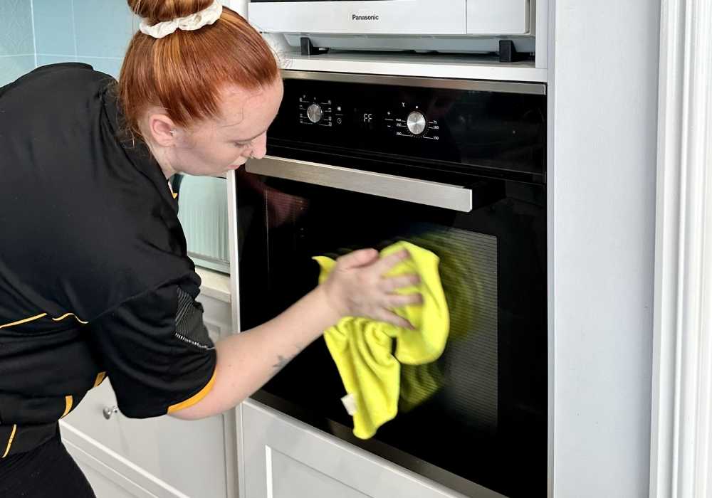 house-cleaner-cleaning-oven-door-glass Maid2Match professional house cleaner cleaning the outside of an oven door glass part during an oven clean